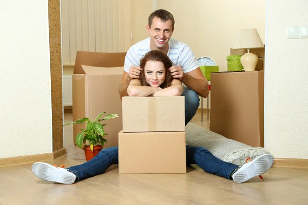 Young couple with boxes in new home on room background — Stock Photo, Image