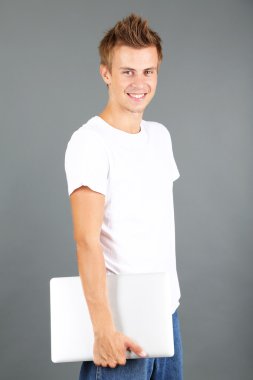 un joven guapo con portátil sobre fondo gris