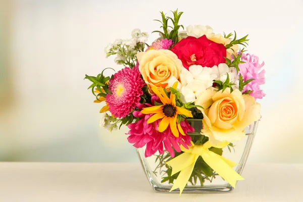 Beautiful bouquet of bright flowers in glass vase, on wooden table, on bright background — Stock Photo, Image