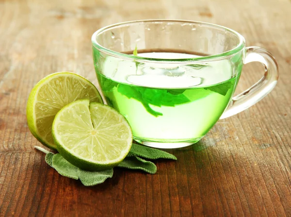 Taza transparente de té verde con lima y salvia sobre fondo de madera — Foto de Stock