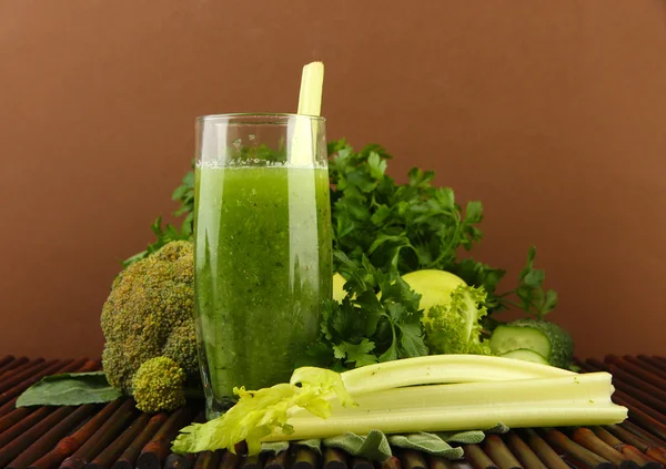 Glasses of green vegetable juice and vegetables on bamboo mat on brown background — Stock Photo, Image