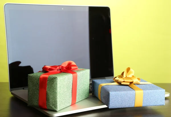 Laptop with gifts on table on green background — Stock Photo, Image