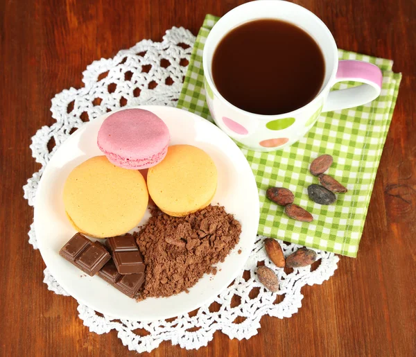 Cocoa in cup with sweets and cocoa powder on plate on wooden table — Stock Photo, Image