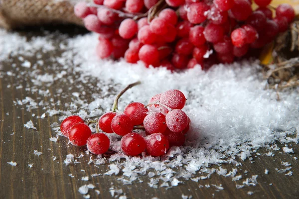 Red berries of viburnum and snow on sackcloth napkin, on wooden background — Stock Photo, Image