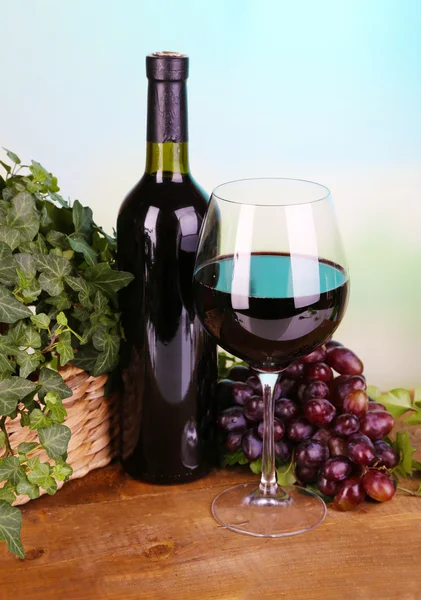 Ripe green and purple grapes in basket with wine on wooden table on bright background — Stock Photo, Image