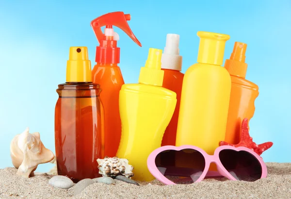 Botellas con crema bronceadora y gafas de sol, sobre fondo azul —  Fotos de Stock