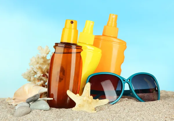 Bouteilles avec crème solaire et lunettes de soleil, sur fond bleu — Photo