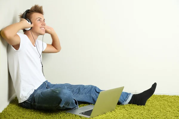 Junger Mann entspannt auf Teppich und hört Musik, auf grauem Wandhintergrund — Stockfoto