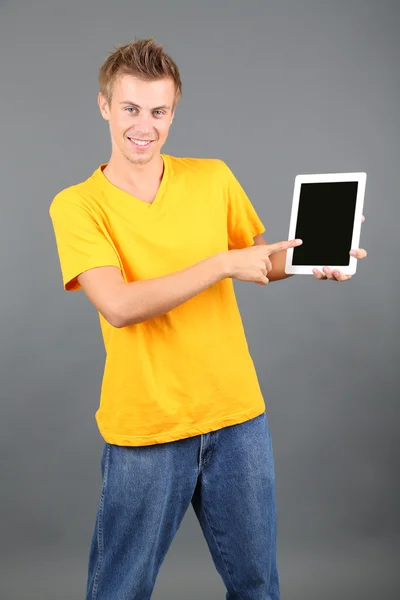 Ein hübscher junger Mann mit Tablette auf grauem Hintergrund — Stockfoto