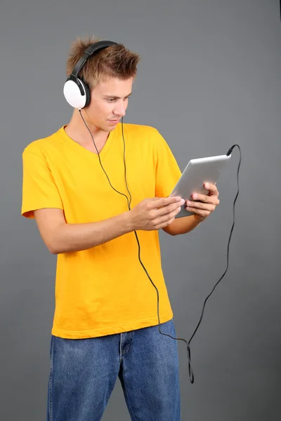 Handsome young man listening to music on grey background — Stock Photo, Image