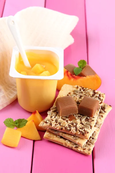 Yogurt gustoso con pezzi di frutta fresca, biscotti e caramelle caramelle caramellate su sfondo di legno a colori — Foto Stock