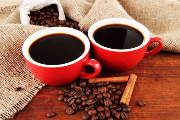 Red cups of strong coffee and coffee beans on table on sackcloth background — Stock Photo, Image