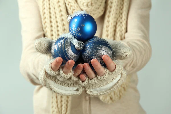 Weibliche Hände in Fäustlingen Weihnachtsbaumkugeln, auf farbigem Hintergrund — Stockfoto