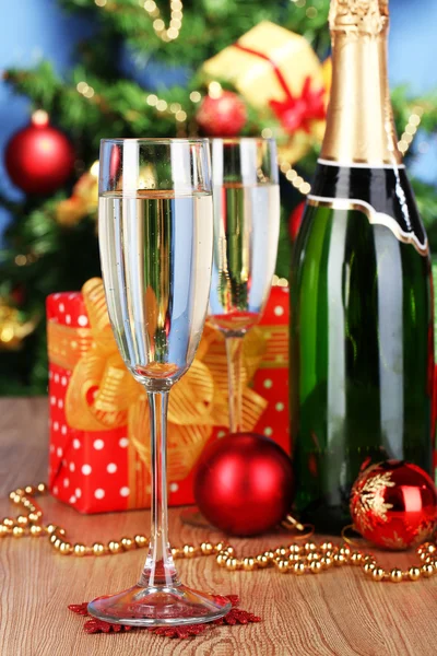 Bottle of champagne with glasses and Christmas balls on wooden table on Christmas tree background — Stock Photo, Image