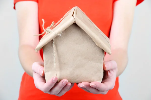 Manos de mujer sosteniendo una casa envuelta en papel kraft marrón — Foto de Stock