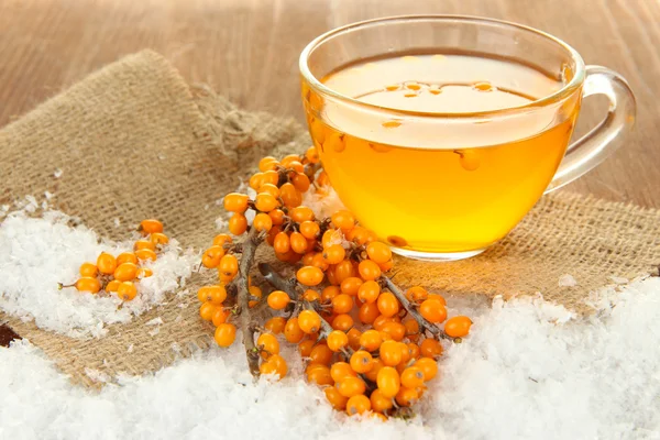 Branches of sea buckthorn with tea and sackcloth on wooden background — Stock Photo, Image