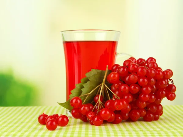 Red berries of viburnum and cup of tea on tablecloth on bright background — Stock Photo, Image