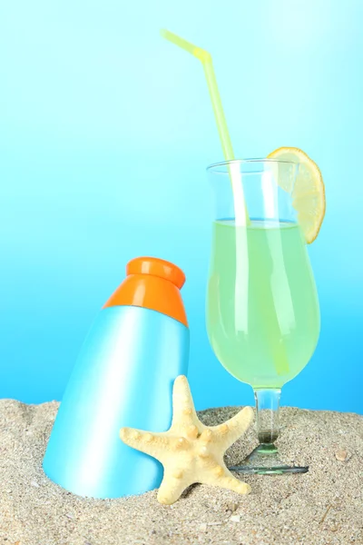 Strand cocktail en zonnebrandcrème in zand op blauwe achtergrond — Stockfoto