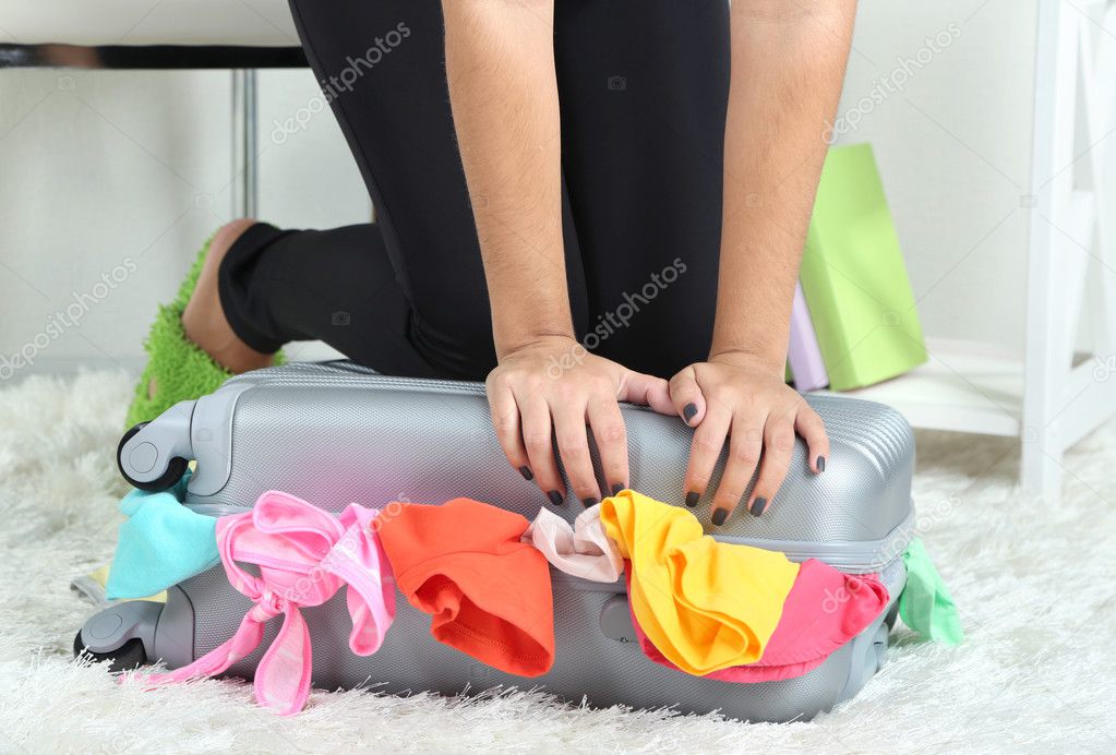 Suitcase with clothes on carpet on room background