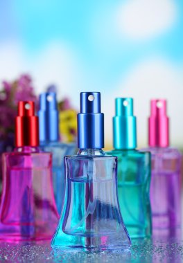 Women perfume in beautiful bottles and flowers on blue background clipart