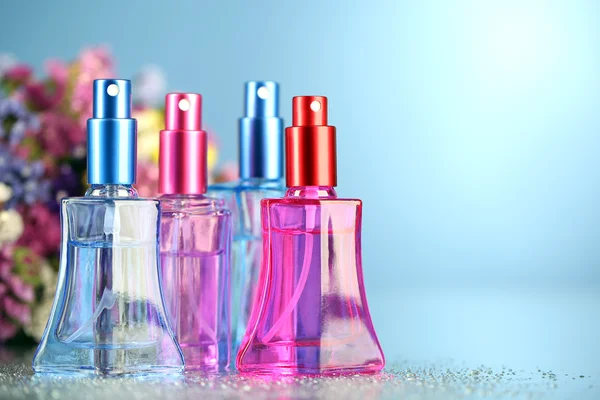 Women perfume in beautiful bottles and flowers on blue background — Stock Photo, Image