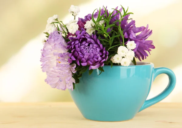 Beau bouquet de fleurs lumineuses en tasse de couleur, sur table en bois, sur fond lumineux — Photo