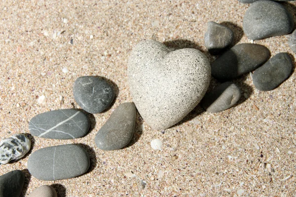 Piedra gris en forma de corazón, sobre fondo de arena — Foto de Stock