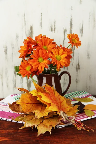 Όμορφη Φθινοπωρινά φύλλα με λουλούδια στο τραπέζι σε ξύλινα φόντο — Φωτογραφία Αρχείου
