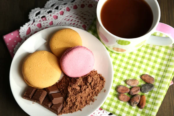 Kakao im Becher mit Süßigkeiten und Kakaopulver auf Teller auf Holztisch — Stockfoto