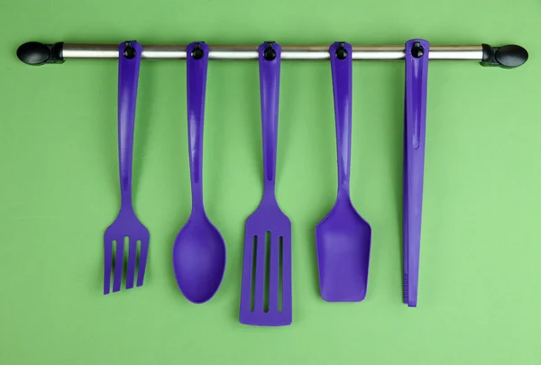 Plastic kitchen utensils on silver hooks on green background — Stock Photo, Image