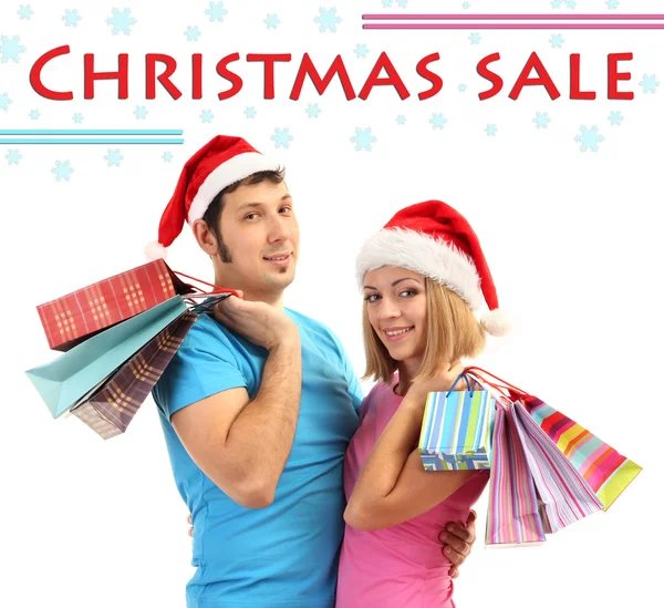 Young couple in Santa hats shopping and holding many shopping bags isolated on white — Stock Photo, Image