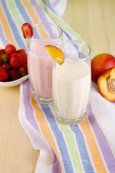 Pyszne koktajle mleczne z truskawkami i brzoskwinia na drewniany stół szczegół — Zdjęcie stockowe