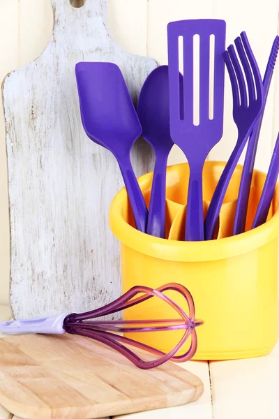 Utensílios de cozinha de plástico em copo na mesa de madeira — Fotografia de Stock