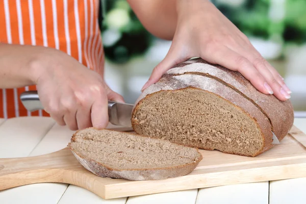 Cutting bread on wooden board on wooden table on window background — Stock Photo, Image