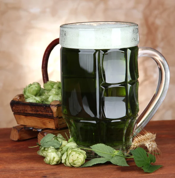 Glass of green beer and hops, on wooden table — Stock Photo, Image