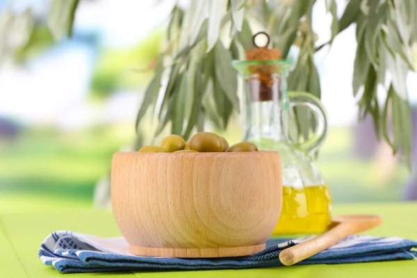 Ελαιόλαδο και ελιές σε μπολ σε χαρτοπετσέτα στο ξύλινο τραπέζι σε φόντο φύση — Φωτογραφία Αρχείου
