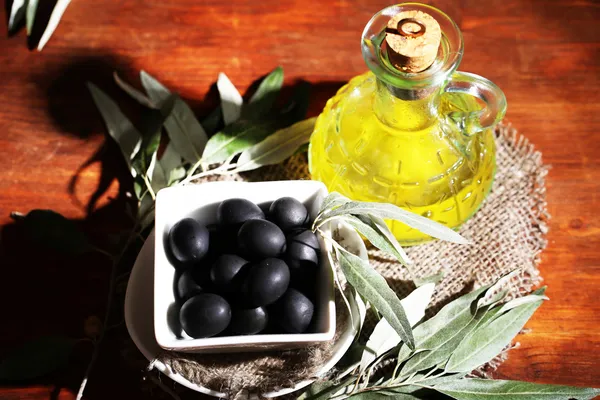 Olivenöl und Oliven in Schüssel auf Sacktuch auf Holztisch — Stockfoto
