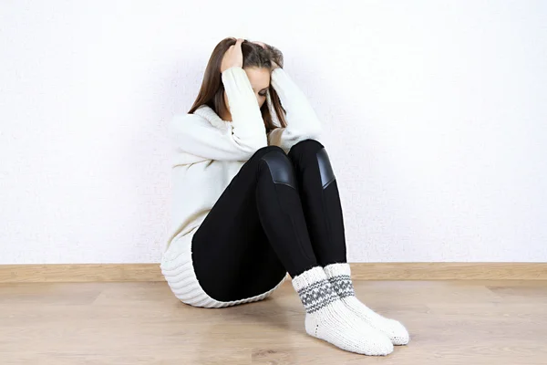Smutna kobieta siedzi na podłodze w pobliżu ściany — Zdjęcie stockowe