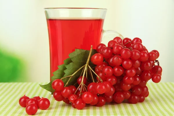 Red berries of viburnum and cup of tea on tablecloth on bright background — Stock Photo, Image