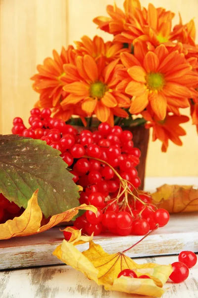 Bayas rojas de viburnum y jarrón con flores en la mesa sobre fondo de madera —  Fotos de Stock
