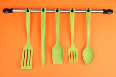 Turuncu arka planda gümüş kancalarda plastik mutfak aletleri.