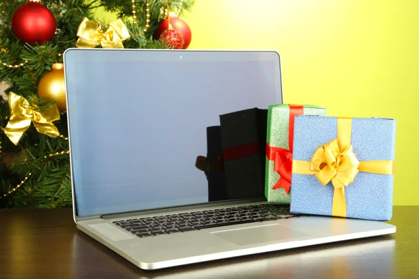 Laptop with gifts on table on green background — Stock Photo, Image