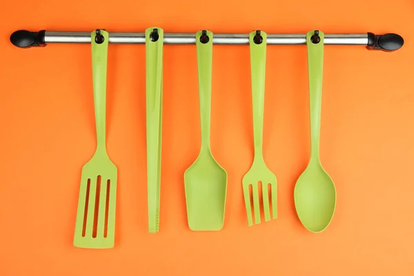 Plastic kitchen utensils on silver hooks on orange background — Stock Photo, Image