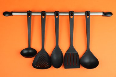 Turuncu arka planda gümüş kancalarda plastik mutfak aletleri.