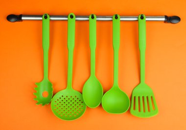 Turuncu arka planda gümüş kancalarda plastik mutfak aletleri.