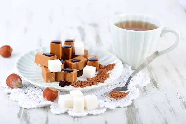 Many toffee on plate and cup of tea on napkin on wooden table — Stock Photo, Image