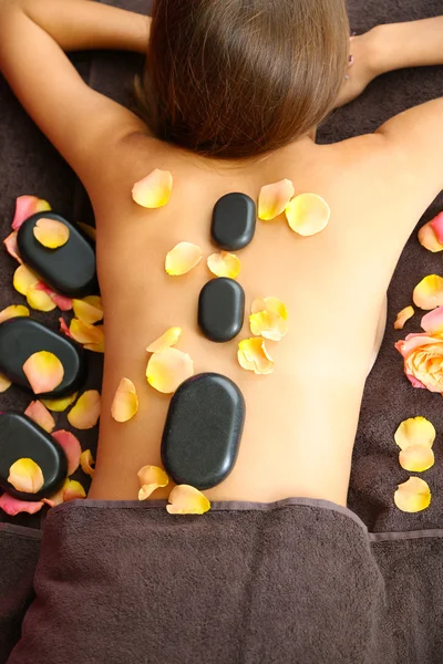 Beautiful young woman having stone massage in spa salon on color background — Stock Photo, Image