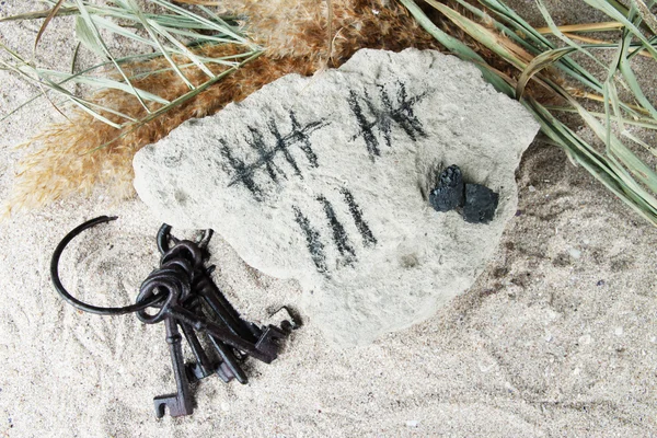Counting days by drawing sticks on stone with keys on sand background — Stock Photo, Image