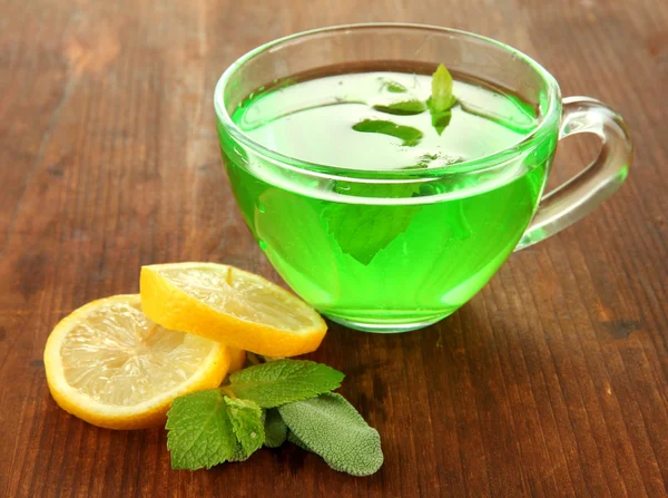 Taza transparente de té verde con limón y menta sobre fondo de madera —  Fotos de Stock