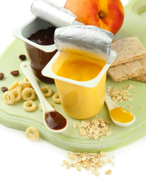 Desserts savoureux dans des tasses en plastique ouvert et peignes de miel, fruits et flocons sur planche de bois isolé sur blanc — Photo